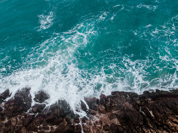 Aerial view of crashing waves on rocks. Background texture of a rocky shore and blue and turquoise sea - Fotoğraf, Görsel