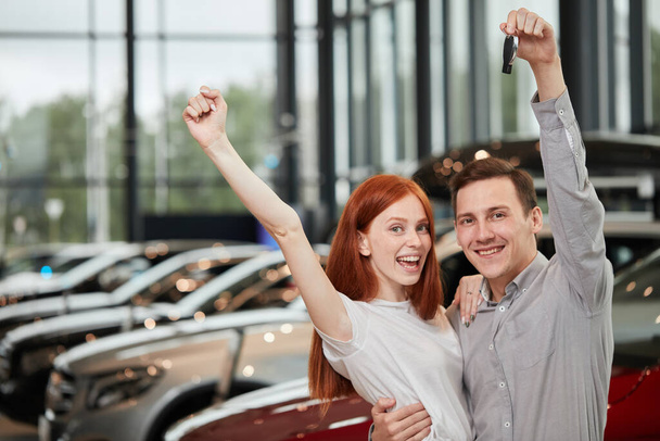 Beautiful couple is holding key of their new car, looking at camera and smiling - Foto, Bild