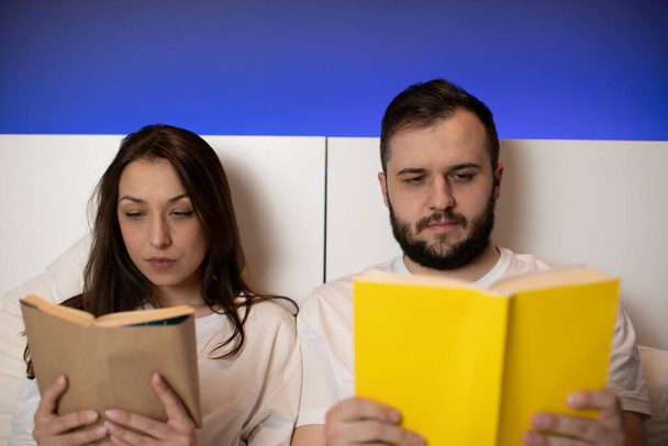 couple of lovers wearing white pajamas focused on reading books in bed - Fotó, kép
