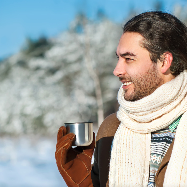 young man with tea standing in snowy woods - Zdjęcie, obraz