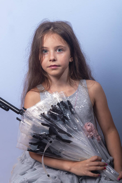 A beautiful long-haired girl with her favorite items in her hands on a light background in a gray dress with sequins. Foreground. Portrait shooting. Quarantine, games at home. - Photo, Image