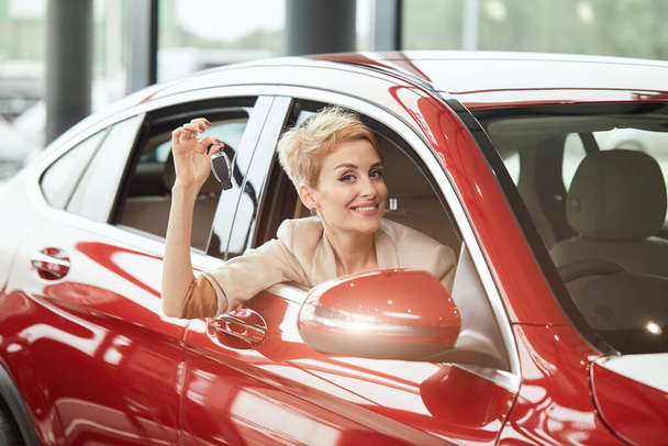 Overjoyed driver woman smiling and showing new key while sitting in car showroom - Photo, Image