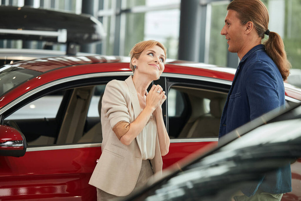 Happy young wife asking to buy a new car for her in the dealership. - Zdjęcie, obraz