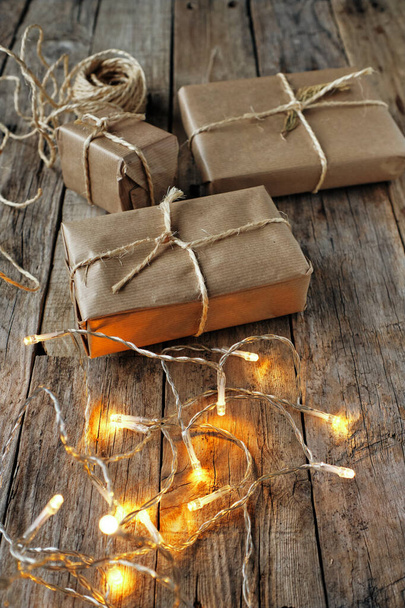 Подарункові пакети, загорнуті крафт-папером і зав'язані мотузкою з лампочками на сільському столі
 - Фото, зображення