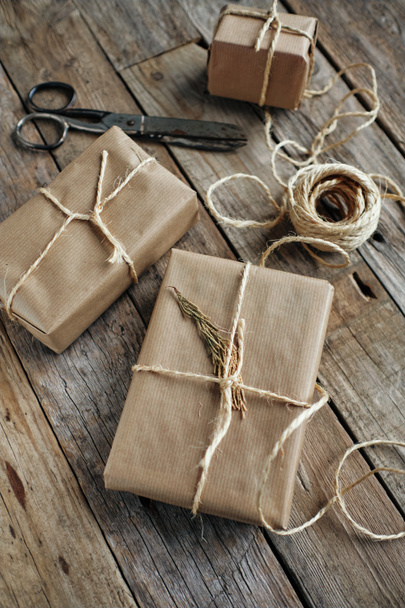Geschenkpakete mit Kraftpapier umwickelt und mit Seil auf rustikalem Holztisch gebunden - Foto, Bild