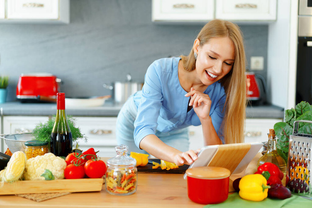 Young beautiful caucasian woman cooking and using her digital tablet in kitchen - Foto, afbeelding