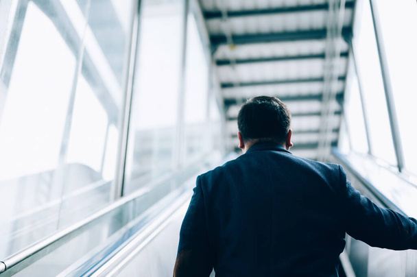Азиатский бизнесмен в костюме и едет вверх по эскалатору на станции метро во время утренней поездки - Фото, изображение