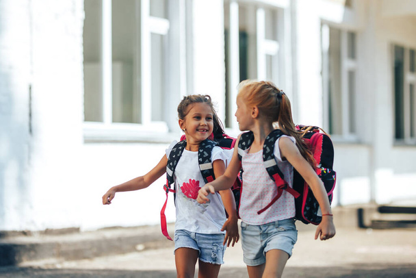 Две школьницы, держа друг друга за руки, бегут из школы, обратно в школу, начальное образование детей. - Фото, изображение