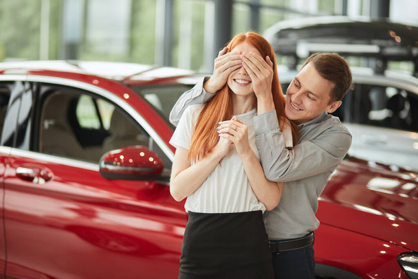 Мужчина делает сюрприз своей жене, покупает ей новую машину в автосалоне. - Фото, изображение