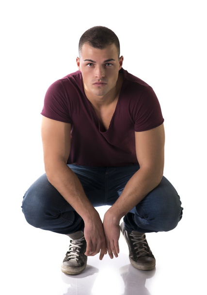 Handsome young man with t-shirt and jeans sitting on his heels - Фото, изображение