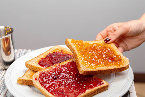 Crispy toasts covered with fruit jam served on kitchen table - Zdjęcie, obraz