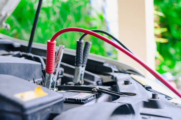 Бустерные кабели и разряженный аккумулятор, зарядка аккумулятора автомобиля с электрическим корытом перемычки кабелей - Фото, изображение