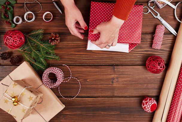 Kobiece dłonie pakujące świąteczny prezent na ciemnym drewnianym tle. - Zdjęcie, obraz