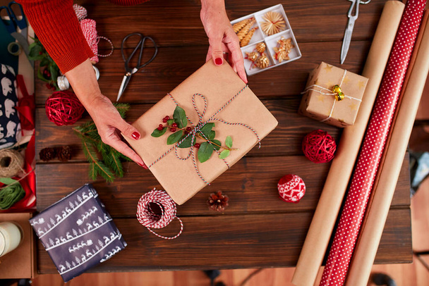 Woman wrapping gift box with decorating items on wood table, close up, top view. - Foto, immagini