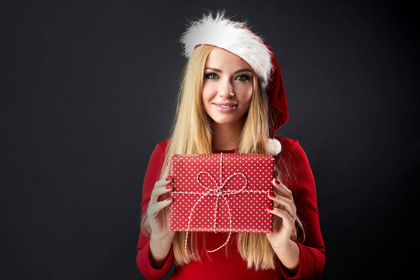 Молодая счастливая женщина в Рождество Санта шляпа держит новогодний подарок изолированы над черным - Фото, изображение
