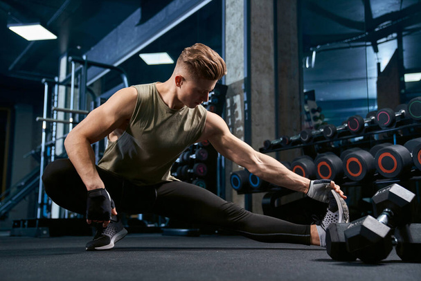Bodybuilder stretching upper body in gym. - 写真・画像