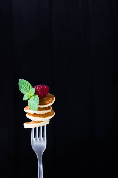 Mini pancakes, pancake cereal on a fork with raspberry and mint on a black background - Foto, Imagem