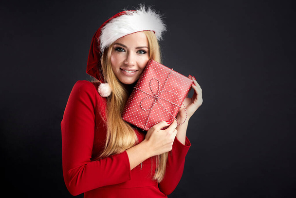 Young happy woman in Christmas Santa hat holds new year gift isolated over black - Foto, Imagem