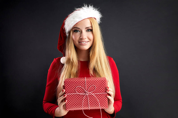 Young happy woman in Christmas Santa hat holds new year gift isolated over black - Фото, изображение