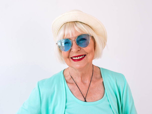 anziana (vecchia) elegante donna allegra in cappello di paglia e occhiali da sole e vestiti turchese. Estate, viaggi, anti età, gioia, pensionamento, concetto di libertà - Foto, immagini