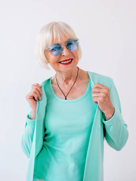 senior stylish cheerful woman in blue sunglasses and turquoise clothes. Summer, travel, anti age, joy, retirement, freedom concept - Photo, Image