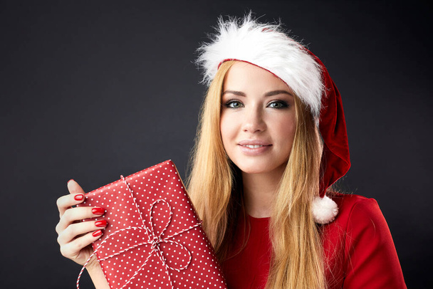 Молода щаслива жінка у Різдвяному капелюсі тримає новорічний подарунок ізольованим над чорним. - Фото, зображення