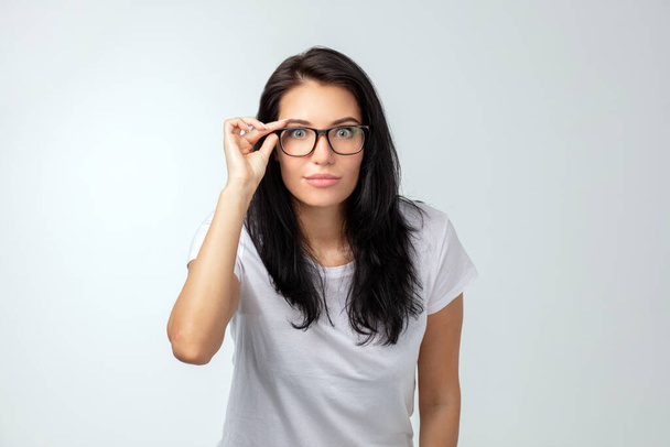 Shocked pretty woman touching her glasses and looking at the camera - Foto, Bild