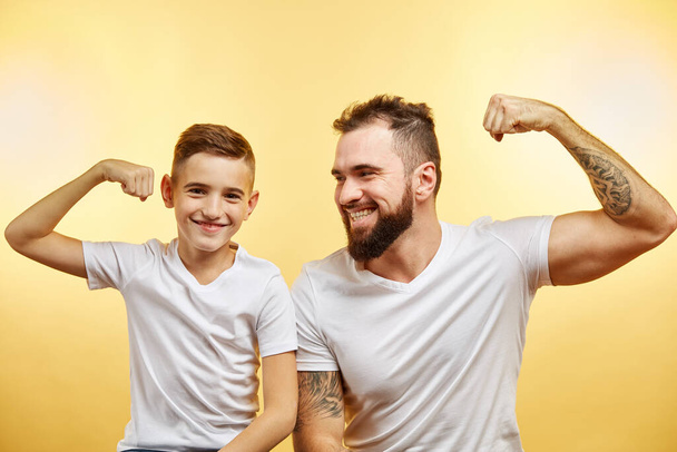 bearded father and his son looking at camera and smiling while show biceps - Photo, image