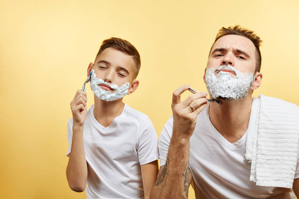 Father and son shaving on yellow background - Foto, imagen