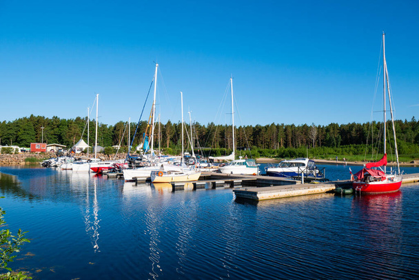Yacht club, with a lot of different yachts and boats, ships. Beautiful nature, green forest in the background. A beautiful red yacht in the foreground. - Photo, Image