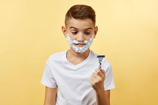 shoking boy preparing for shaving face over yellow background - 写真・画像