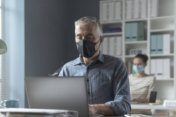 オフィスでのコロナウイルスの予防と社会的距離:ビジネスの人々の安全距離を維持し、顔のマスクを着て、コロナウイルスの予防の概念 - 写真・画像