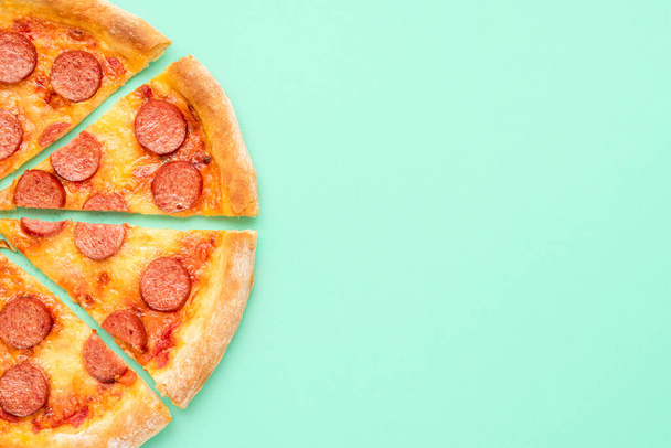 Yeşil arkaplanlı pepperonili pizzayla üst tarafta. Yeşil renkli bir masada dilimlenmiş pizza. Ev yapımı pizza. - Fotoğraf, Görsel