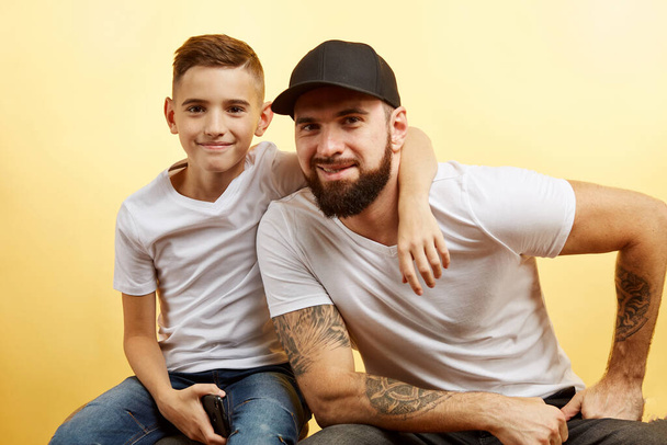 bearded father and little son smile for camera on yellow background - Foto, immagini