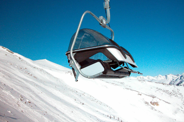 chairlift in alpine ski area, clear blue sky, mountain slope covered in snow - Photo, Image