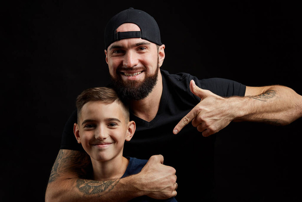 bearded father and little son smile for camera on black background - Foto, Bild