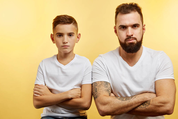 father and son sitting together against yellow background. Quarrel, resentment, insult, offense concept - Фото, зображення