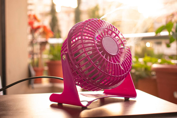 Рожевий міні-вентилятор, що працює на відкритому повітрі на дерев'яному столі
 - Фото, зображення
