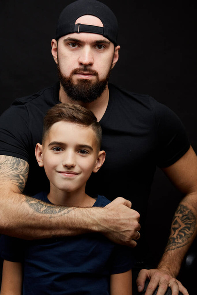 bearded father and little son smile for camera on black background - Фото, зображення