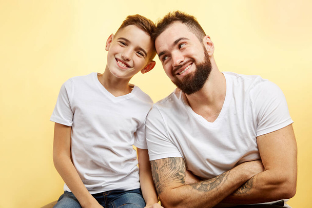 bearded father and little son smile for camera on yellow background - Фото, зображення