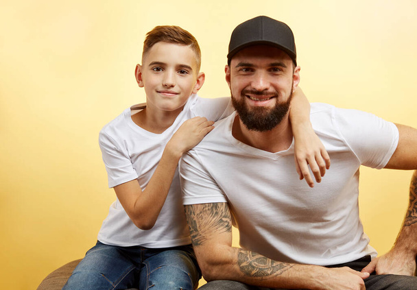 padre barbuto e piccolo figlio sorriso per fotocamera su sfondo giallo - Foto, immagini