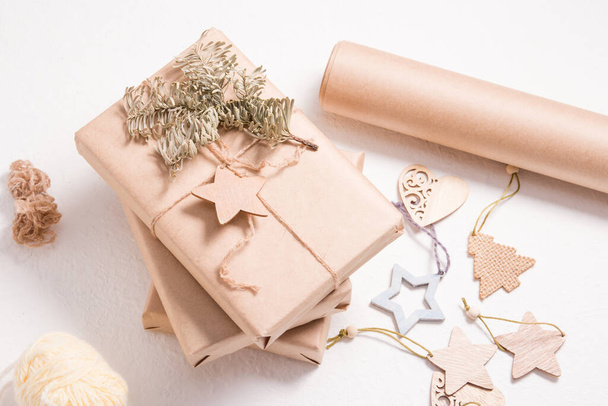 eco friendly gift box packaging for christmas or new year, wooden christmas toys, box wrapped in kraft paper with a spruce branch and a wooden star on a white background - Fotografie, Obrázek