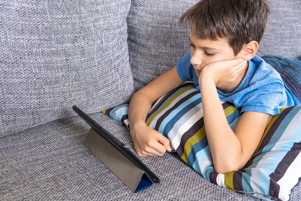 少年は自宅のデジタルタブレットコンピュータとソファに横たわっていた。技術、ダンス教育、オンライン学習、ゲームのコンセプトをプレイ - 写真・画像