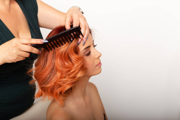 Beautiful redhead woman getting her hair comb by professional female hairdresser.  - Photo, Image