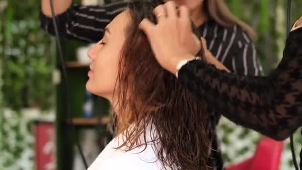 A girl hairdresser makes a client keratin hair straightening. The girl is sitting in beauty salon. Using a hairdryer. Social distance. Protective measures   - Footage, Video