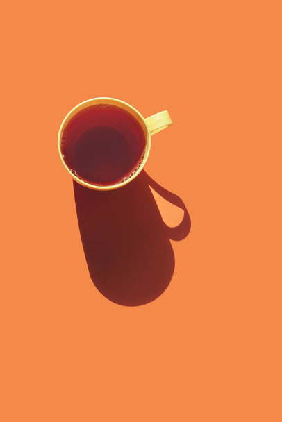 tè caldo in una tazza di plastica gialla sullo sfondo arancione. immagine di luce dura e ombre profonde con spazio per il testo  - Foto, immagini