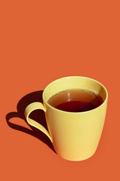chá quente em uma xícara de plástico amarelo contra fundo laranja. luz dura e sombras profundas imagem com espaço para texto  - Foto, Imagem