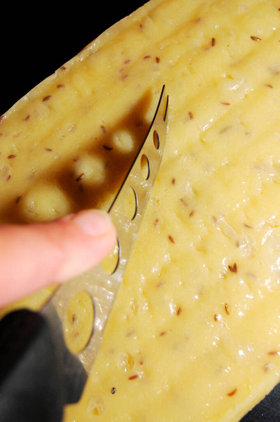découper un fromage avec des graines de cumin avec un couteau à fromage - Photo, image