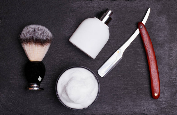 Lâmina, escova, perfume, bálsamo e espuma de barbear em um fundo preto
. - Foto, Imagem