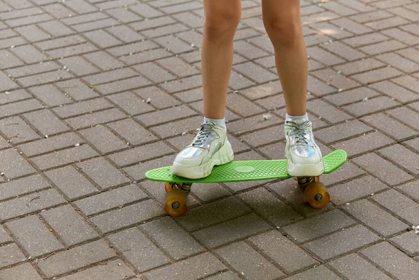 Close-up of legs in bright sneakers that stand on a green skateboard. - Fotoğraf, Görsel